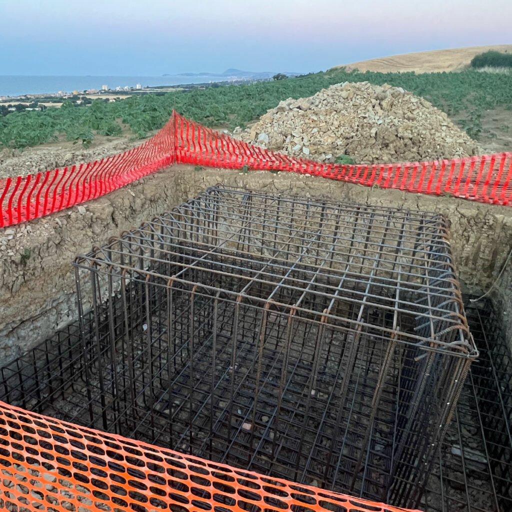 La griglia d'acciaio nel buco già scavato. Sullo sfondo la collina e il mare