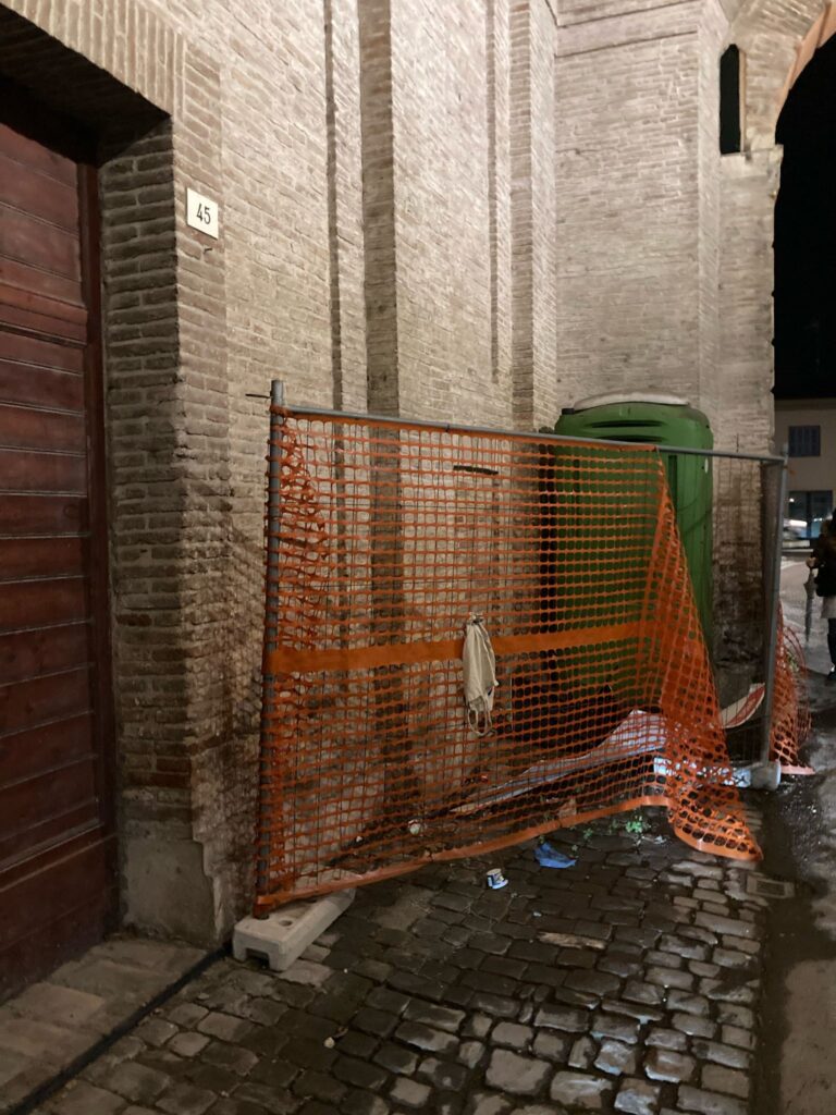 Sotto l'arco della Porta, un lato è occupato da resti di cantiere e un bagno chiico abbandonato